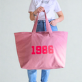 Person holding a pink tote bag with '1986' printed on it against a plain background