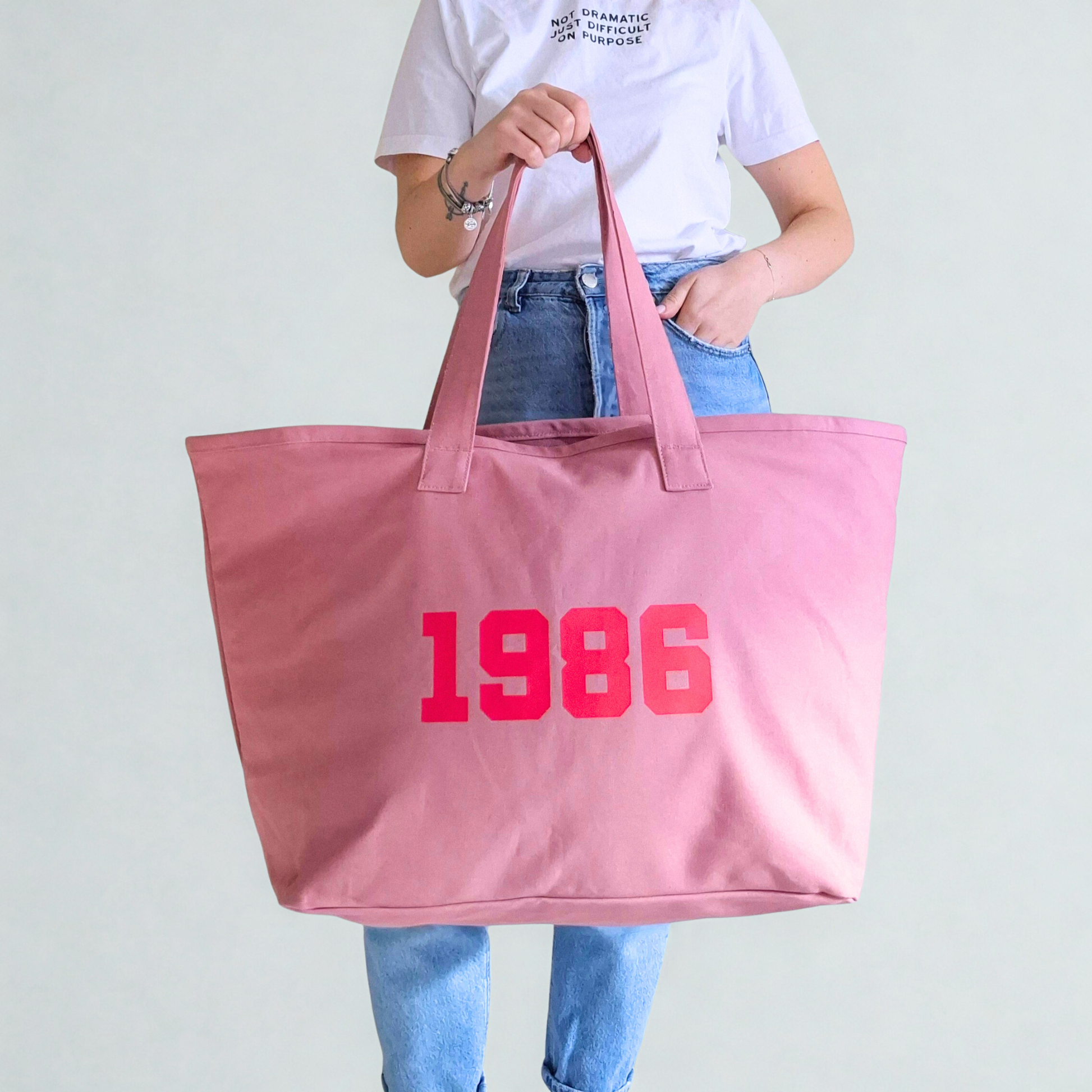 Person holding a pink tote bag with '1986' printed on it against a plain background