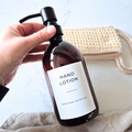 Hand holding a brown hand lotion bottle with a pump, labeled 'Hand Lotion' from the Bathroom Collection.