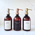 Three bottles of hand wash, washing up liquid, and hand lotion with pump dispensers on a white marble surface.