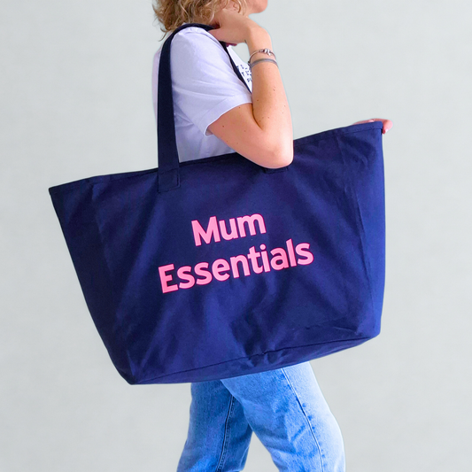 Person holding a navy tote bag with 'Mum Essentials' text on a plain background