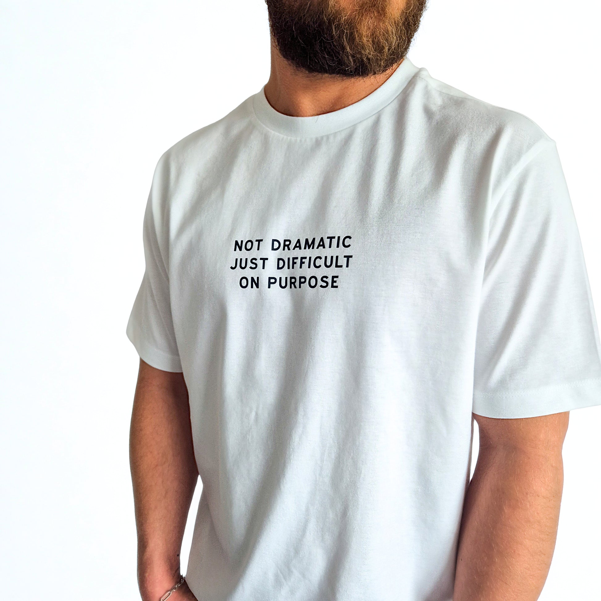 White t-shirt with text 'Not  dramatic just difficult on purpose' worn by a person on a white background