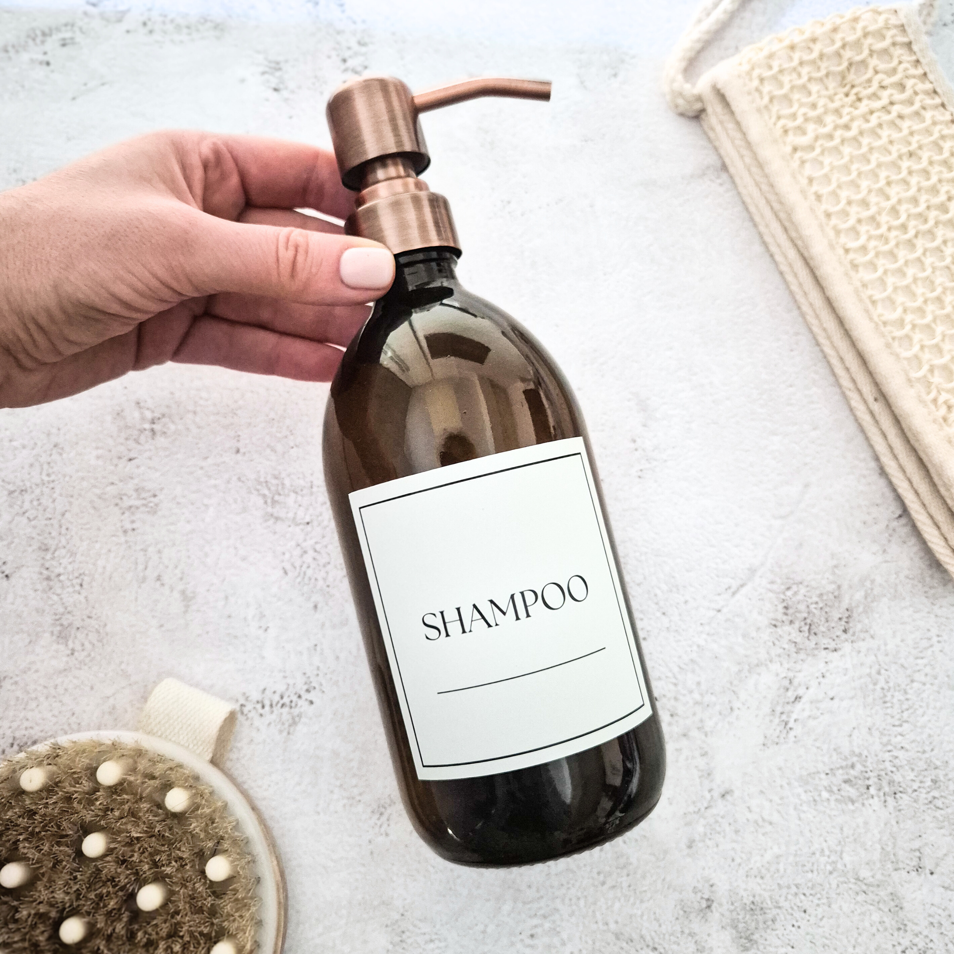 Hand holding a shampoo bottle with a pump on a light background