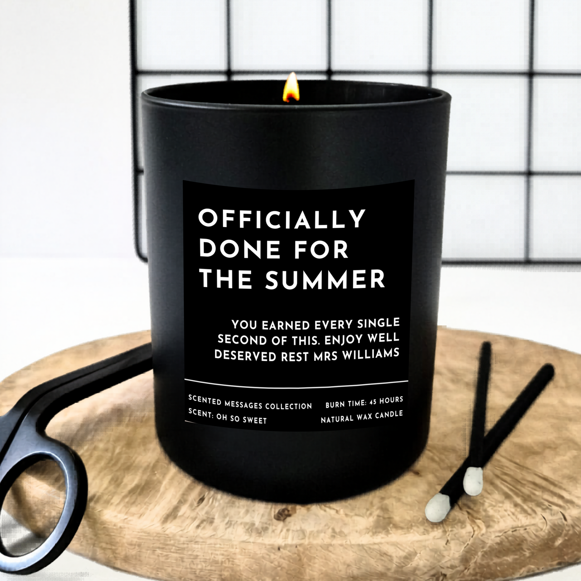 Black candle with text  'Officially done for the summer' and a personalised message underneath 'you earned every single of this. Enjoy well deserved rest Ms Williams'. on a wooden board with matches.