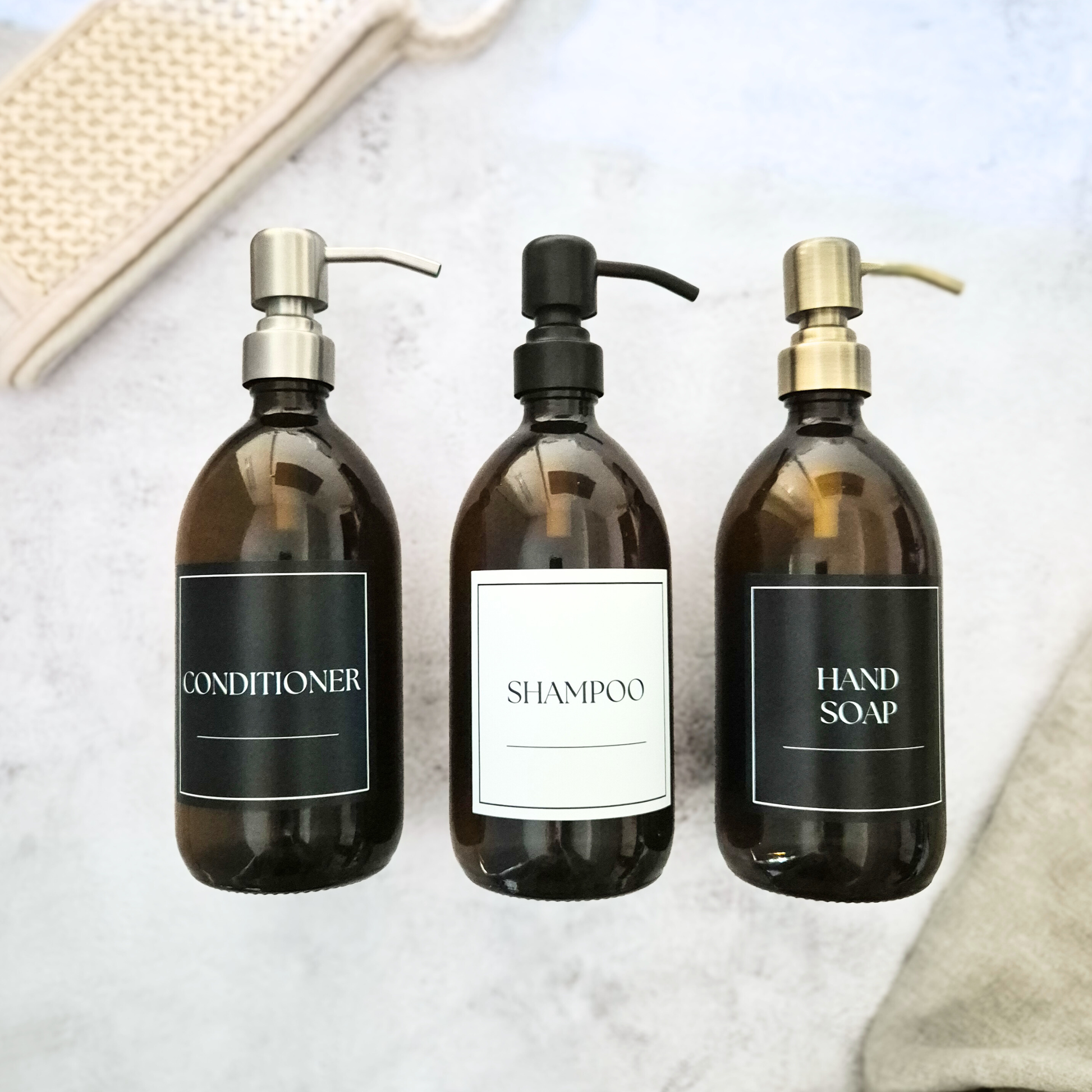 Three amber bottles labeled 'Conditioner', 'Shampoo', and 'Hand Soap' on a light background.