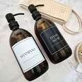 Two amber refillable bottles labeled 'Shampoo' and 'Hand Soap' on a textured surface.