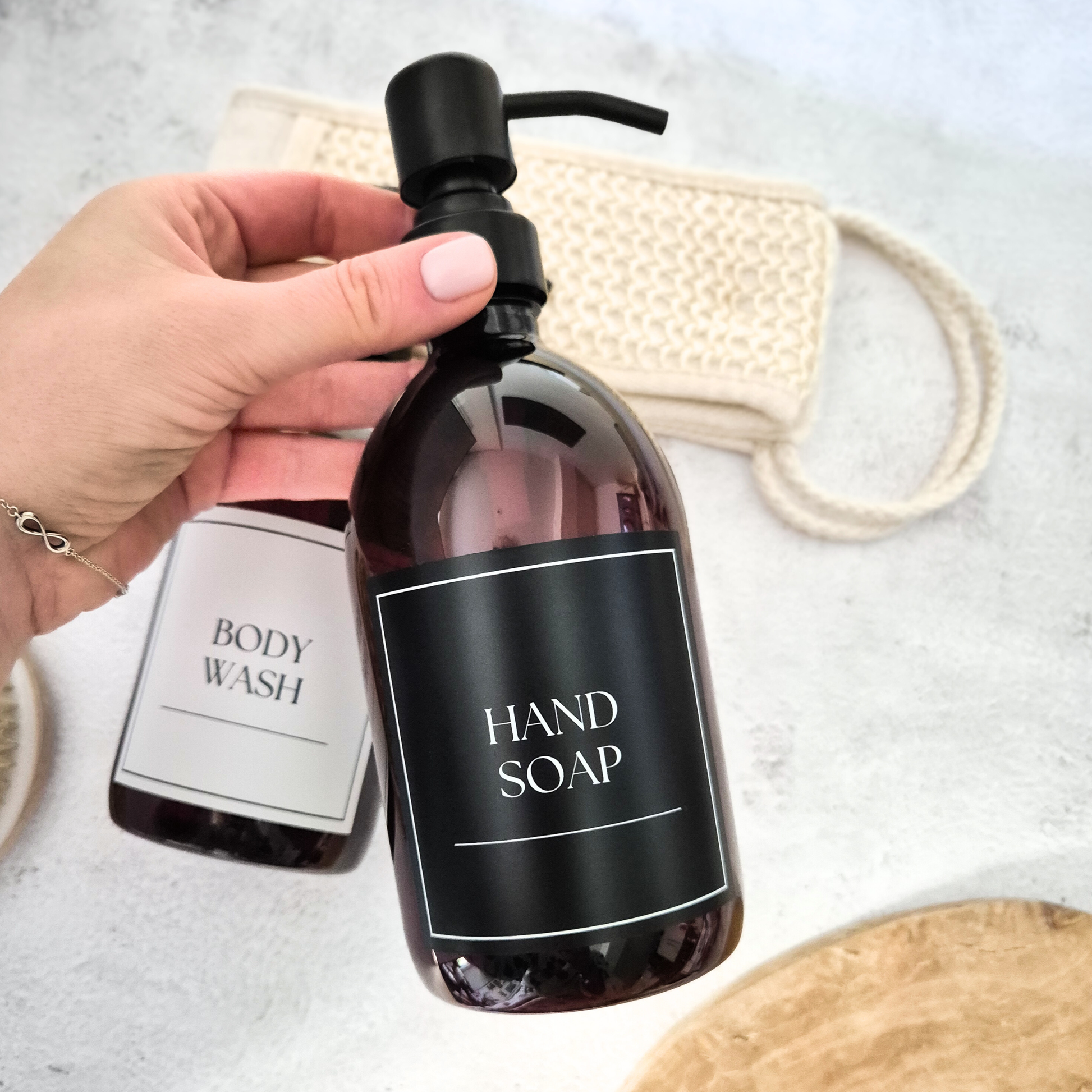 Hand soap bottle with pump held by a hand on a light background