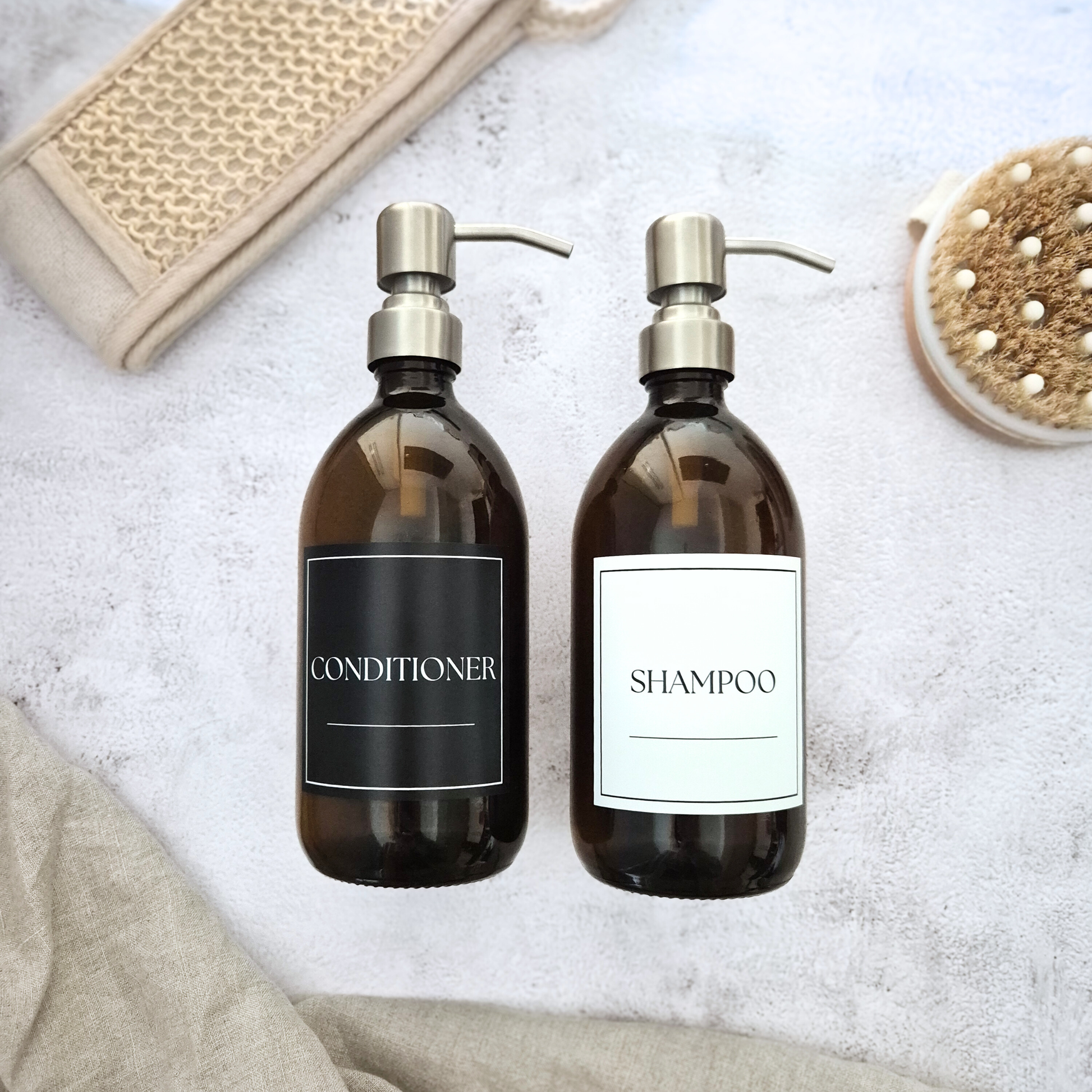 Twoamber bottles labeled 'Shampoo' and 'Conditioner' on a textured surface.
