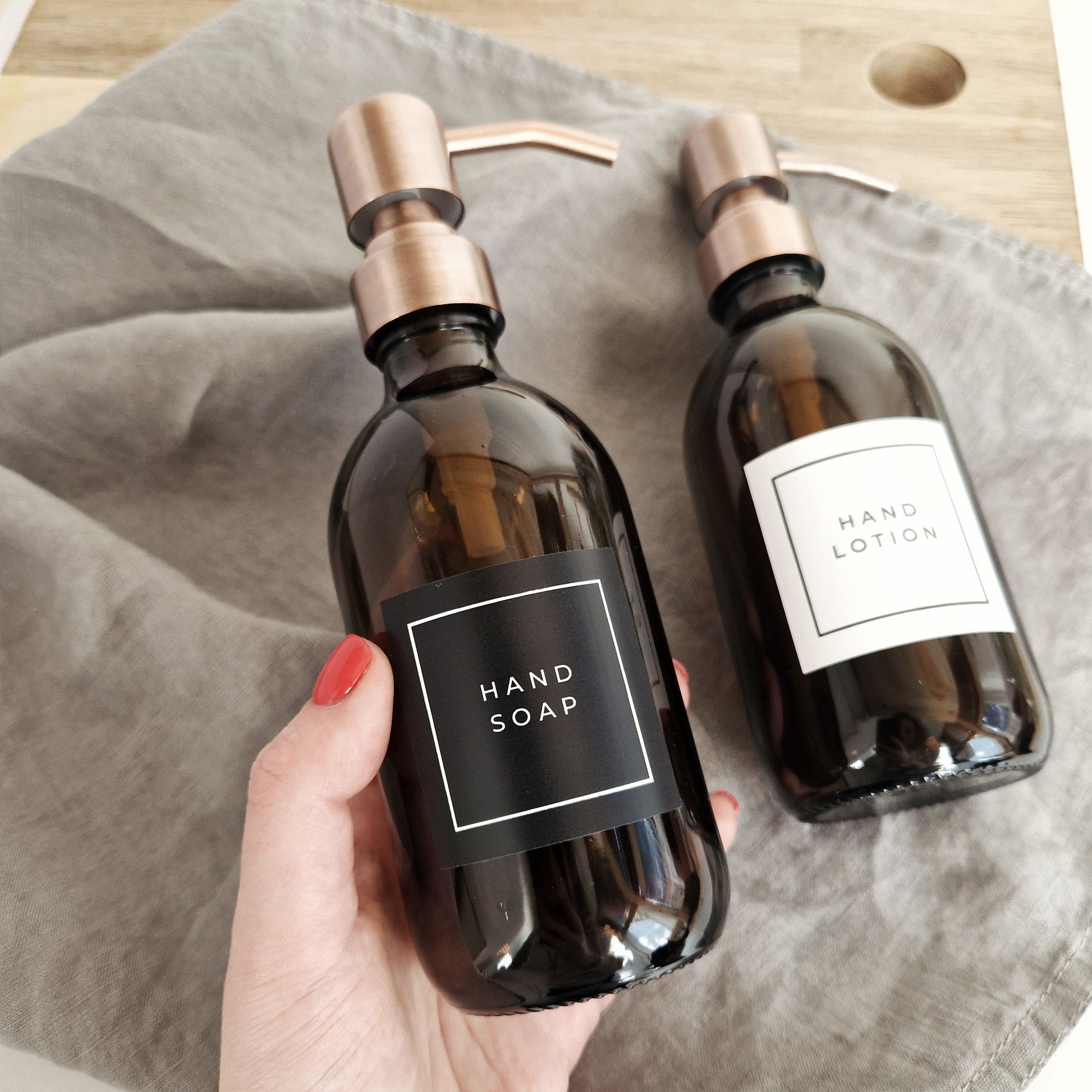 Two brown bottles labeled 'Hand Soap' and 'Hand Lotion' on a gray surface.