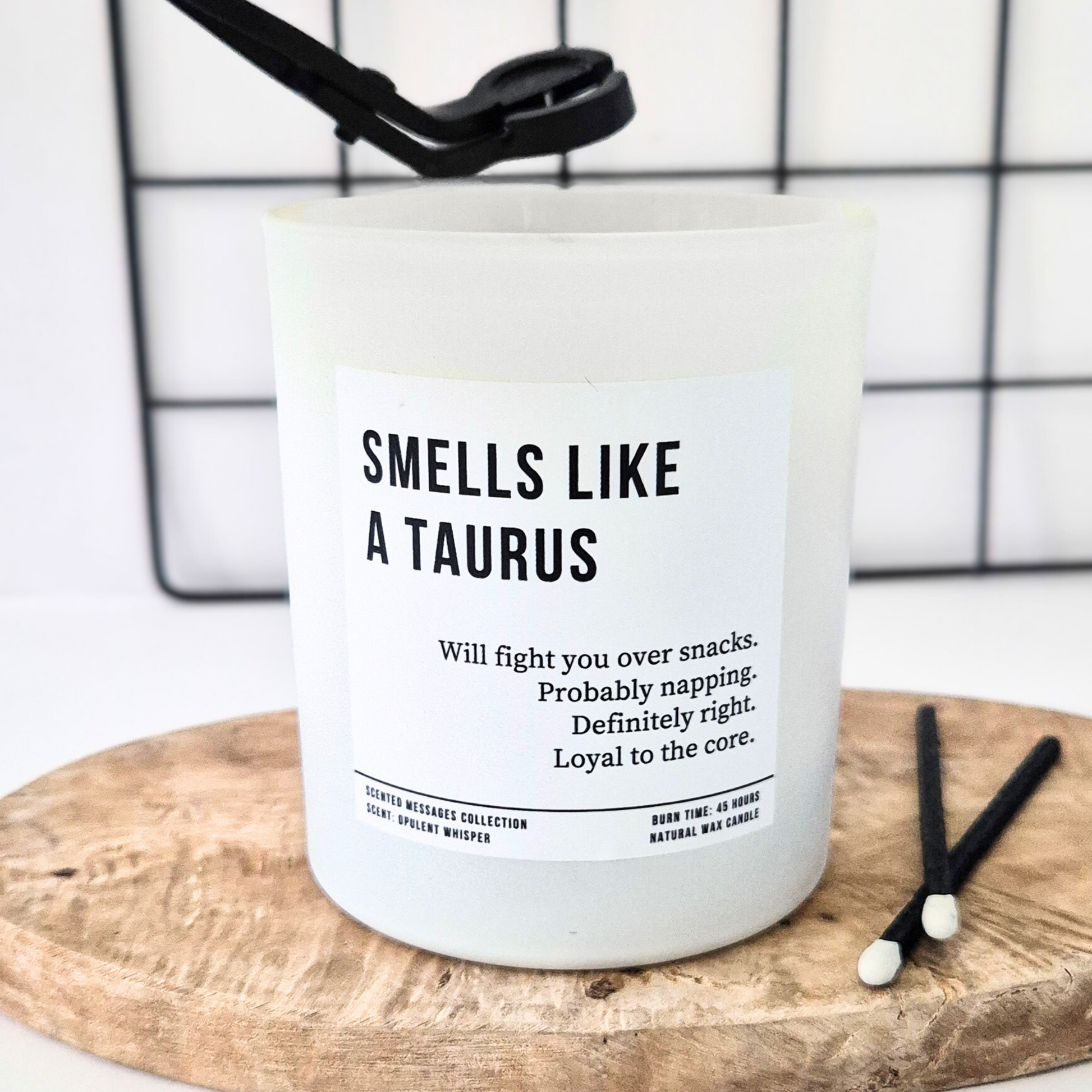 Candle with text 'Smells like a Taurus' with a personalised message on a wooden board against a white background