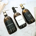 Three amber bottles labeled 'Conditioner', 'Shampoo', and 'Hand Soap' on a textured surface.