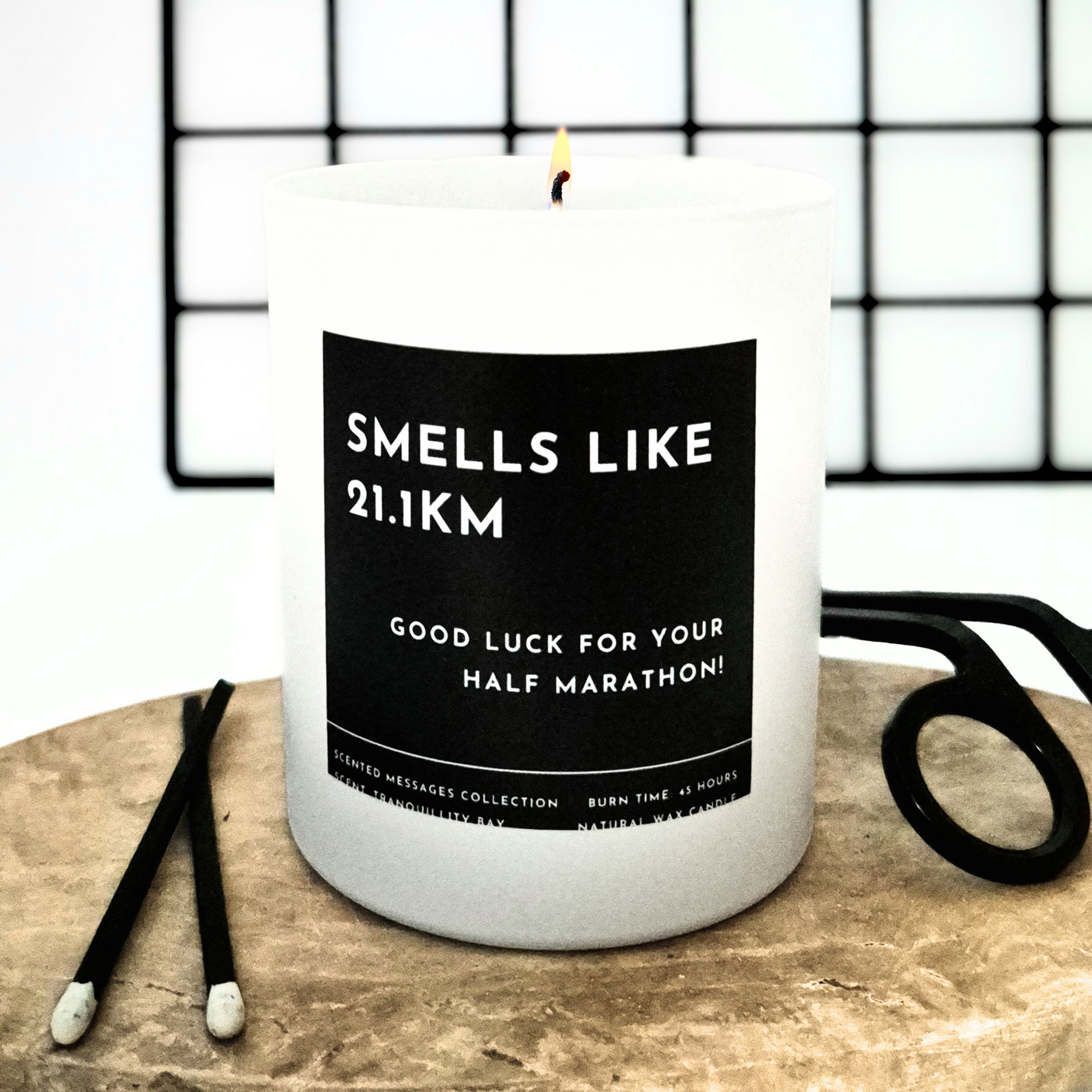 Candle with a label 'Good luck for your half marathon' and a personalised message on a wooden surface with scissors in the background