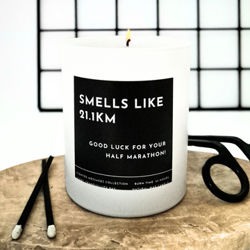 Candle with a label 'Good luck for your half marathon' and a personalised message on a wooden surface with scissors in the background
